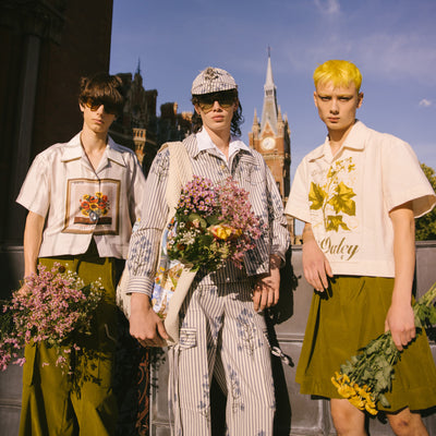 Three men in S.S.Daley clothes, glasses and holding floral arrangements.